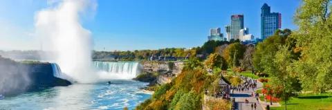 Niagarafälle mit Wasserfontäne neben einem Stadtpark mit Promenade und zwei Wolkenkratzern