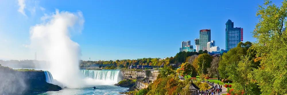 Niagarafälle mit Wasserfontäne neben einem Stadtpark mit Promenade und zwei Wolkenkratzern