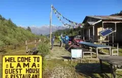 Eine Lodge im nepalesischen Mangengoth mit bunten Fahnen vor einem Bergpanorama ist zu sehen.