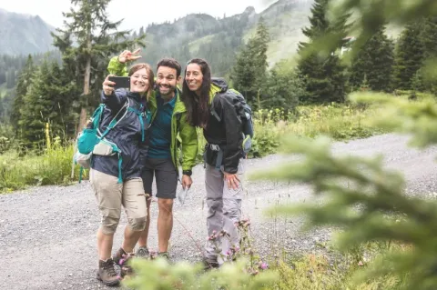 Drei junge Wanderer stehen auf einem Weg und blicken in eine Smartphone-Kamera.