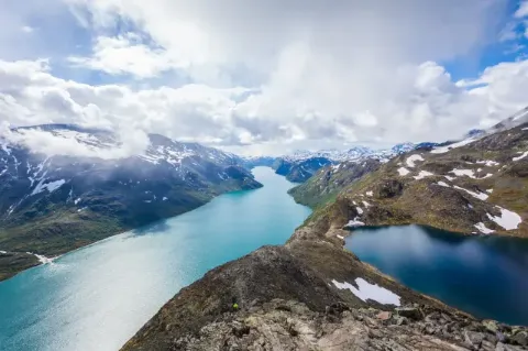 Blick auf eine Fjordlandschaft von oben. Rechts und links neben den Flüssen sind hügelige Landschaften mit Altschneefeldern zu sehen. 
