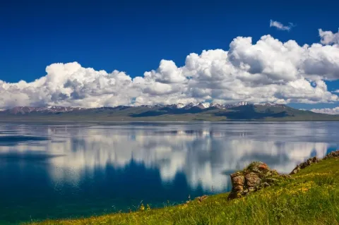 Auf der Oberfläche eines dunkelblauen Sees sind die Spiegelungen der Wolken zu sehen, die am Horizont auftauchen. 