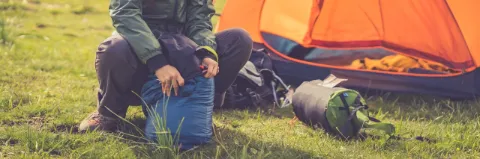Eine Frau sitzt vor ihrem Zelt und räumt ihren Schlafsack auf. 