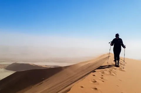 Eine Frau geht mit Stöcken auf einer Sanddüne und hinterlässt Spuren.