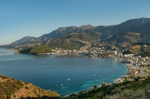 Blick auf eine Bucht mit einer Stadt. Im Hintergrund sind grünbraune Hügel zu sehen. 