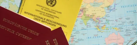 Ein gelber Impfpass und zwei europäische Reisepässe liegen auf einer Landkarte