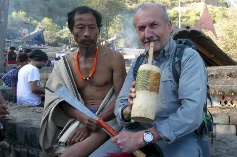 Zwei Männer sitzen auf einer Steinmauer. Der rechte Mann posiert mit einem Trinkbecher aus Holz.