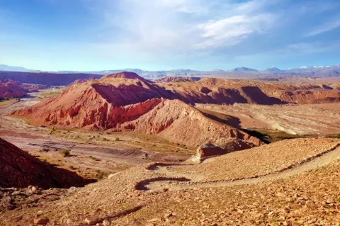 Eine bergige Landschaft in der Wüste. Der Boden ist rötlich gefärbt. 