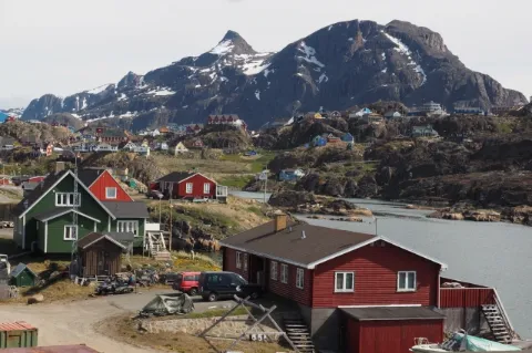 Ein Dorf mit bunten Häusern am Wasser. Dahinter sind teils schneebedeckte Berge.