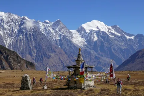 Wanderer stehen um einen buddhistischen Schrein. Im Hintergrund sind schneebedeckte Berge.