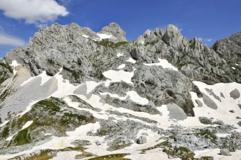 Eine Berglandschaft mit Schneefeldern. Die Felsen sind grau. Der Himmel ist blau.