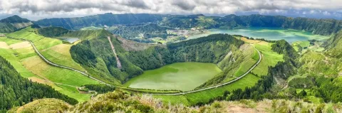 In einem Krater ist ein grün scheinender See. Dahinter sieht man einen weiteren See und ein Dorf.