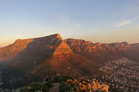 Der Tafelberg ist groß und scheint orange im Abendlicht. Auf der Rechten Seite ist eine Stadt.