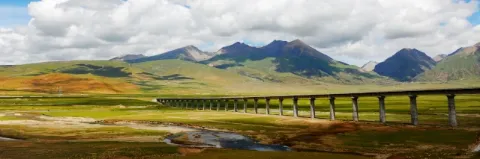 In einer grünen Landschaft mit Bergen und kleinen Wasserlöchern ist eine lange Zugbrücke.