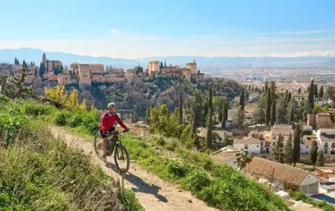 Eine Frau radelt mit ihrem E-Bike auf einer Schotterpiste. Im Hintergrund sieht man eine Stadt und eine Burg.