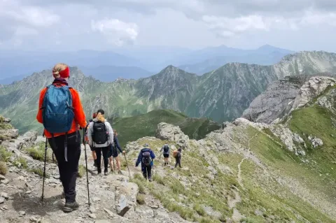 Sechs Personen mit Wanderstöcken laufen hintereinander über einen Grat bei bewölktem Himmel