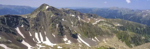 Karge Berglandschaft mit einzelnen Schneefeldern unter blauem Himmel