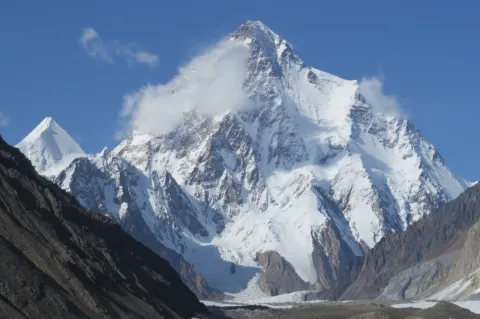 Frontaler Blick auf einen imposanten, schneebedeckten Berggipfel in einer felsigen Umgebung. 