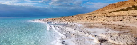 Türkisblaues Wasser, Strand mit weißem Sand und helle, flache Felsenküste unter blauem Himmel