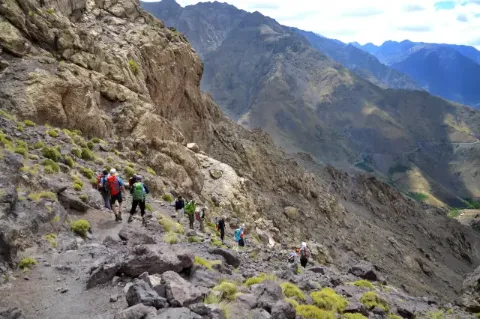 Gruppe von Wanderern läuft Berghang mit Geröll hinauf in einer grauen, felsigen Berglandschaft