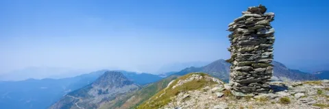 Aufschichtung von Steinen steht am Gipfel in einer Berglandschaft unter blaue Himmel
