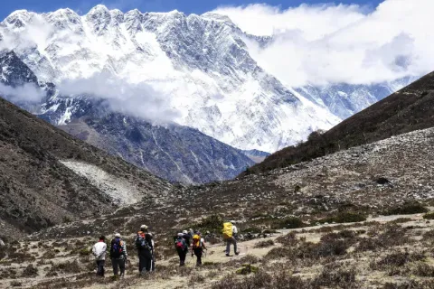 Sechs Wanderer mit Rucksack laufen auf Pfad durch braune Berglandschaft und schneebedeckten Bergen 