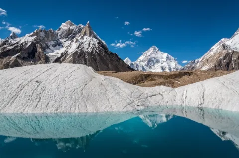 Ein türkiser Gletschersee umgeben von weißen Gletschern. In der Ferne sind schneebedeckte Berge. 