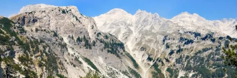 Eine Bergkette aus grauen Stein. Teils sind die Berge von grünen Büschen und Rasen bewachsen.