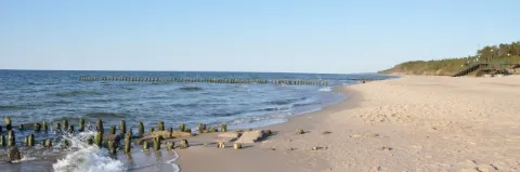 Weißer Sandstrand am Meer mit Brandung und grün bewachsenen Dünen 