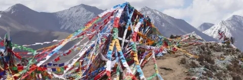 Auf einem Gipfel sind viele bunte Gebetsfahnen gespannt. Im Hintergrund sind hohe Berge.