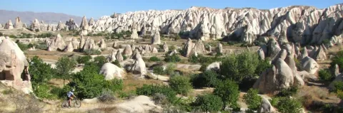 Blick über eine Ebene mit aufragenden Felsspitzen aus hellgrauem Fels. Zwischen den Felsen wachsen grüne Büsche, im Vordergrund steht eine Radfahrerin und blickt über die Ebene. 