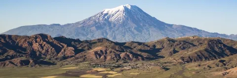 Schneebedeckter Berg erhebt sich aus einer dunkelgrünen Hochebene mit niedriger Bergkette