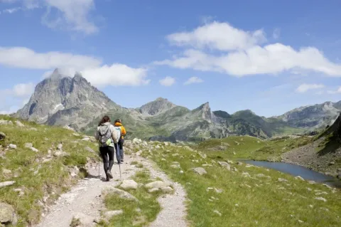 Zwei Wanderer mit Rucksäcken und Wanderstöcken gehen über eine steinige Wiese im Gebirge.