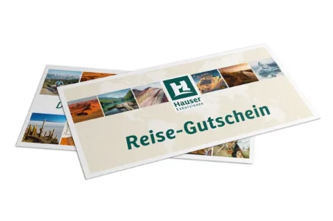 Eine Reisegutschein der Firma Hauser Exkursionen liegt auf weißem Untergrund