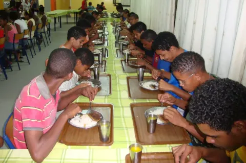 Jungs sitzen entlang eines langen Tisches und essen von Tellern zu Mittag.
