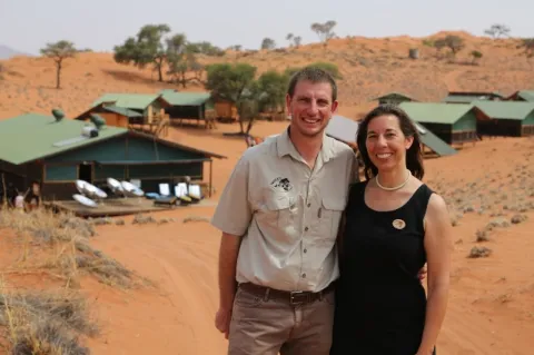 Viktoria und Andreas Keding, Gründer von NaDEET, stehen Arm in Arm vor mehreren Gebäuden in einer kargen Wüstenlandschaft. 