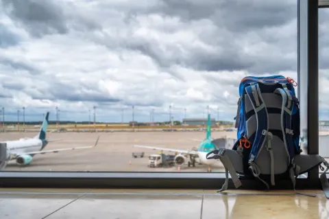 Ein Rucksack steht vor einem großen Fenster mit Blick auf das Außengelände des Flughafens München.