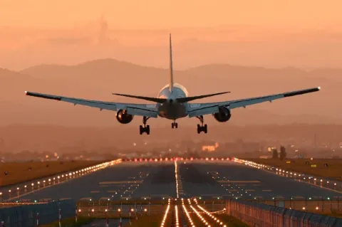 Es ist ein Flugzeug von hinten zu sehen, das im Abendlicht auf einer Landebahn landet.