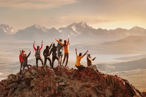 Eine große Gruppe glücklicher Touristen hat Spaß und begrüßt den Sonnenuntergang auf dem Berggipfel.