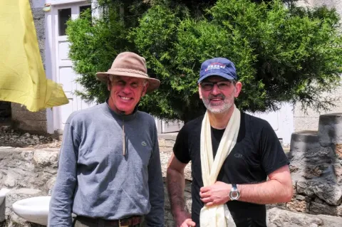 Manfred Häupl und Peter Hillary stehen zur Kamera gewandt und lachen. Im Hintergrund ist eine Haustür und ein kleiner Baum zu sehen.