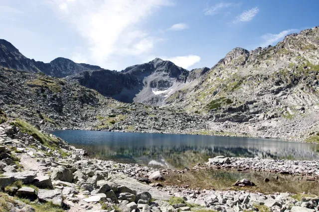 Blick auf einen kleinen, blauen Gebirgssee der in einem felsigen Gelände liegt. Im Hintergrund sind hügelige Felsen zu sehen.