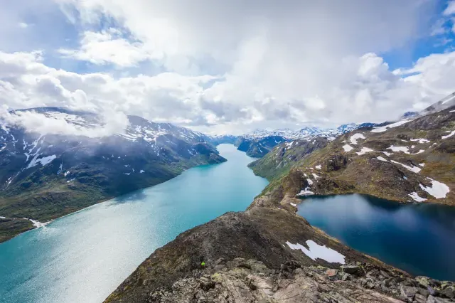 Blick auf eine Fjordlandschaft von oben. Rechts und links neben den Flüssen sind hügelige Landschaften mit Altschneefeldern zu sehen.