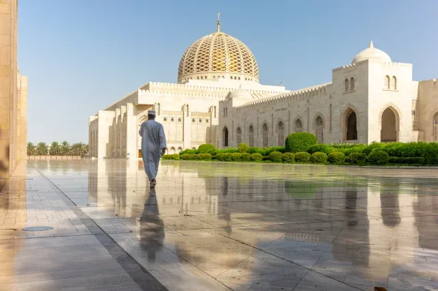 Ein Mann geht auf einem betonierten Untergrund auf eine große weiße Moschee mit goldenen Dach zu.
