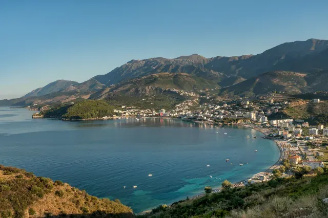 Blick auf eine Bucht mit einer Stadt. Im Hintergrund sind grünbraune Hügel zu sehen.