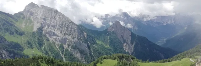 Blick auf die felsige Hügellandschaft der karnischen Alpen, über denen weiße Wolken schweben.