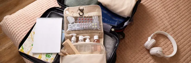 Ein offener Reisekoffer mit Reiseapotheke liegt auf einem Bett