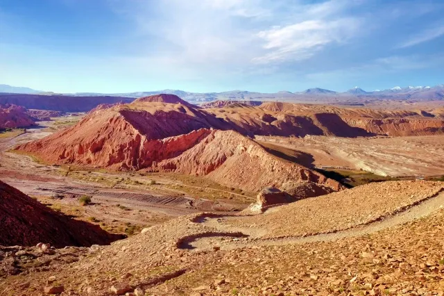 Eine bergige Landschaft in der Wüste. Der Boden ist rötlich gefärbt.