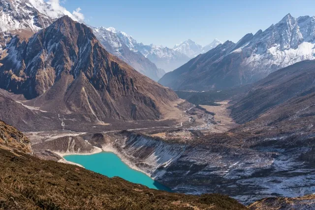 Ein blauer Bergsee in der Mitte. Darum herum sind hohe Gipfel, die teils schneebedeckt sind.