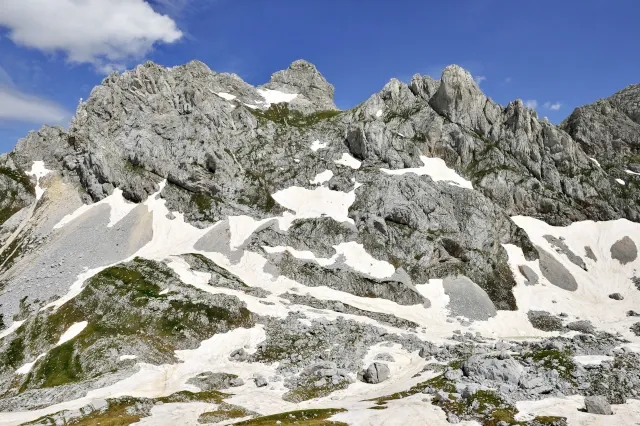 Eine Berglandschaft mit Schneefeldern. Die Felsen sind grau. Der Himmel ist blau.