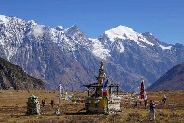 Mehrere Wanderer stehen um einen buddhistischen Schrein. Im Hintergrund sind schneebedeckte Berge.